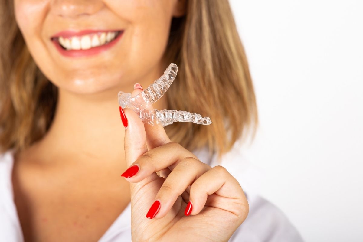 A woman smiling while holding a set of clear Invisalign aligners, illustrating a guide on how often to soak and clean aligners for dental hygiene.